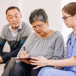 Asian senior couple sitting on a couch with a doctor, discussing health matters in a warm and supportive environment.