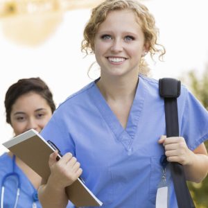 A female nurse smiles while holding a clipboard, showing her friendly and professional demeanor.